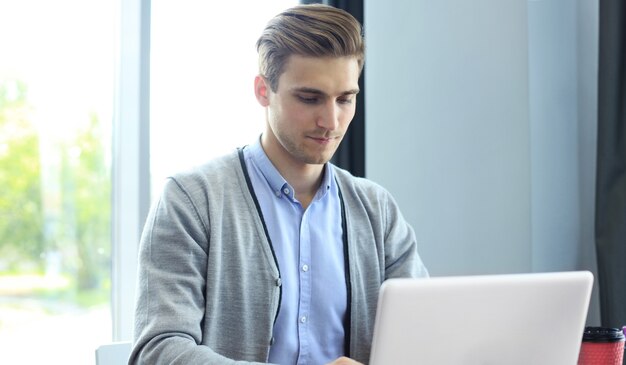 Giovane uomo d'affari moderno che lavora utilizzando il laptop mentre è seduto in ufficio