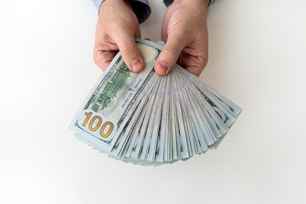Giovane uomo d'affari mostra i soldi in dollari americani vista dall'alto del ricalcolo in contanti su uno sfondo bianco Profitto di un uomo d'affari