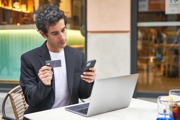 Giovane uomo d'affari multitasking con lo shopping online in un bar che utilizza la tecnologia