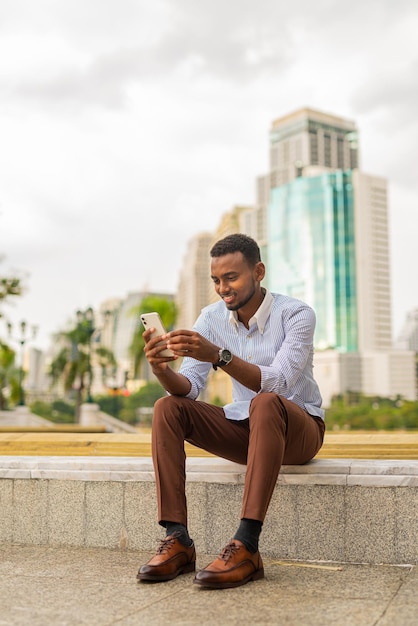 Giovane uomo d'affari nero bello al parco tramite telefono cellulare