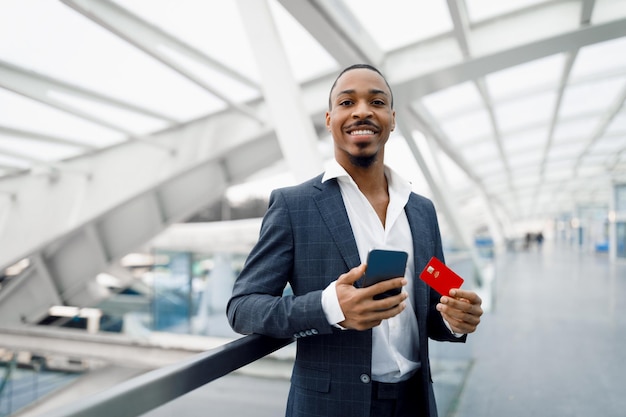 Giovane uomo d'affari nero che utilizza lo smartphone e la carta di credito mentre si trova in aeroporto