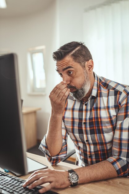 Giovane uomo d'affari pensieroso serio bello sta lavorando al computer in ufficio. È preoccupato per qualcosa che appare sul computer.