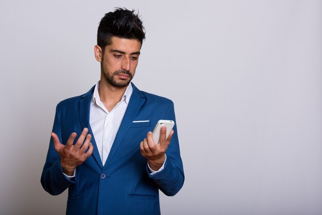 Giovane uomo d'affari persiano barbuto bello in vestito facendo uso del telefono