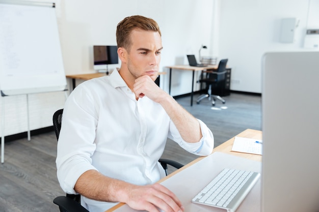 Giovane uomo d'affari premuroso che pensa e usa il computer al lavoro