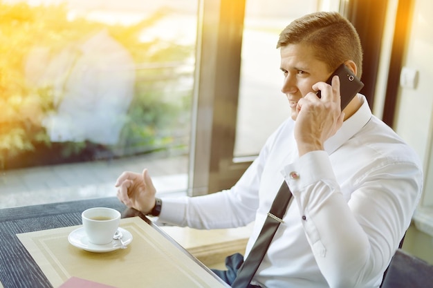 Giovane uomo d'affari seduto al caffè la mattina e parlando al telefono