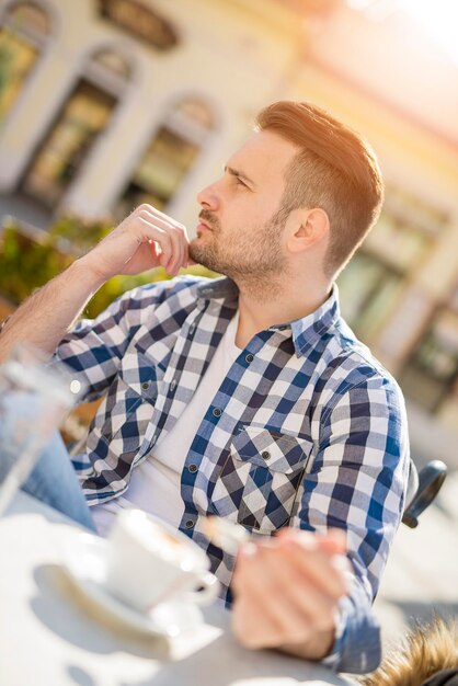 Giovane uomo d'affari seduto in un caffè durante una pausa caffè e distogliendo lo sguardo.