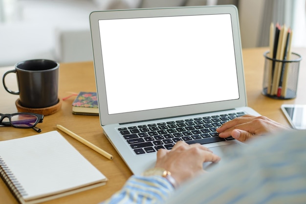 Giovane uomo d'affari seduto in un posto di lavoro confortevole e utilizzando il computer portatile e lo schermo bianco vuoto sulla scrivania con taccuino a matita tazza di caffè e occhiali