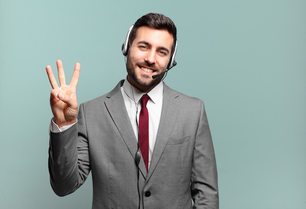 Giovane uomo d'affari sorridente e dall'aspetto amichevole, mostrando il numero tre o il terzo con la mano in avanti, contando il concetto di telemarketing