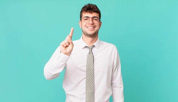 Giovane uomo d'affari sorridente e dall'aspetto amichevole, mostrando il numero uno o il primo con la mano in avanti, conto alla rovescia