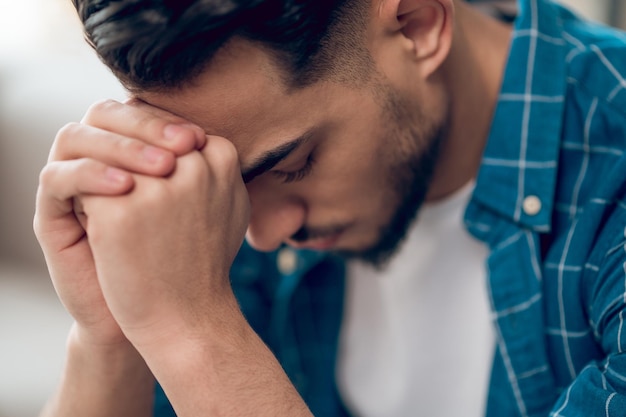 Giovane uomo dai capelli scuri seduto con uno sguardo infelice