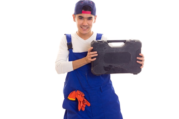 Giovane uomo dall'aspetto elegante in tuta blu con guanti arancioni e cassetta degli attrezzi con snapback in studio