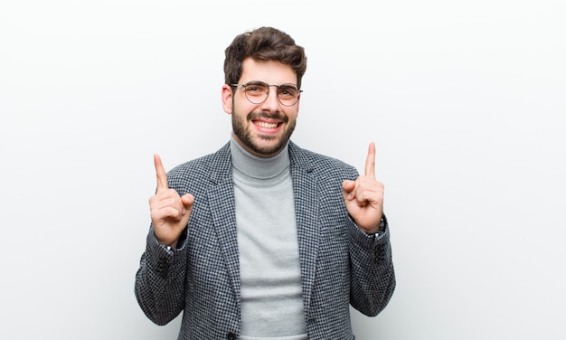 Giovane uomo del gestore che si sente stupito e con la bocca aperta che punta verso l'alto con uno sguardo scioccato e sorpreso contro il bianco