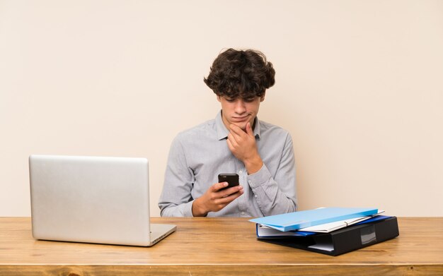 Giovane uomo dello studente con un computer portatile che pensa e che invia un messaggio