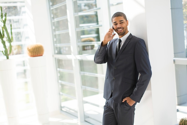 Giovane uomo di colore bello con il telefono cellulare nell&#39;ufficio