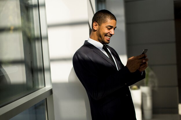 Giovane uomo di colore bello con il telefono cellulare nell&#39;ufficio