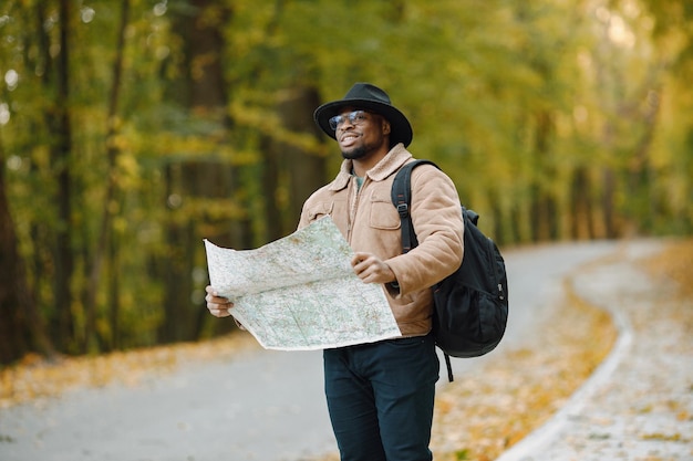 Giovane uomo di colore che fa l'autostop sulla strada e tiene una mappa. Viaggiatore maschio che si sente perso, viaggia da solo in autostop