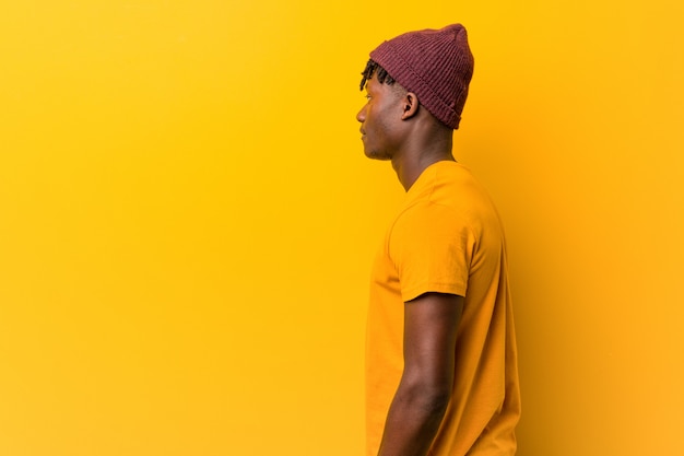 Giovane uomo di colore che indossa rasta sopra giallo guardando a sinistra, posa laterale.