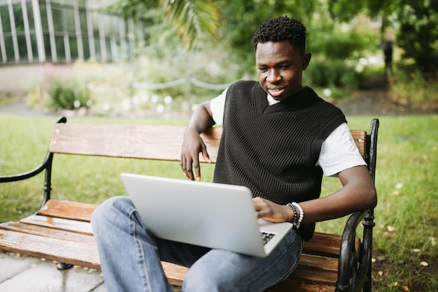 Giovane uomo di colore che lavora al computer portatile all'aperto guardando lo schermo sorridente