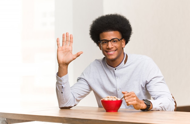 Giovane uomo di colore che mangia una prima colazione che mostra numero cinque