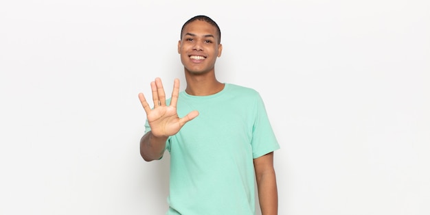 Giovane uomo di colore che sorride e sembra amichevole, mostrando il numero cinque o quinto con la mano in avanti, contando alla rovescia