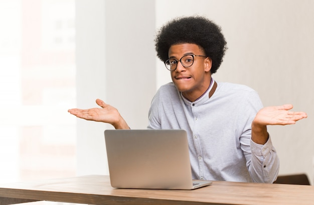 Giovane uomo di colore che usando il suo computer portatile confuso e dubbioso