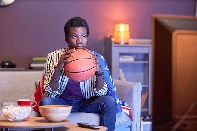 Giovane uomo di colore come appassionato di sport che guarda la partita di basket in TV a casa