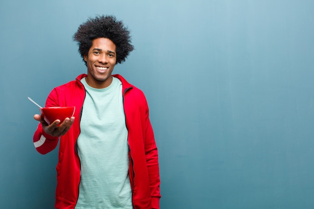 Giovane uomo di colore con una ciotola per la colazione sulla parete blu del grunge