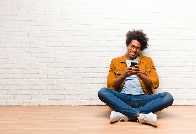 Giovane uomo di colore con uno smart phone seduto sul pavimento