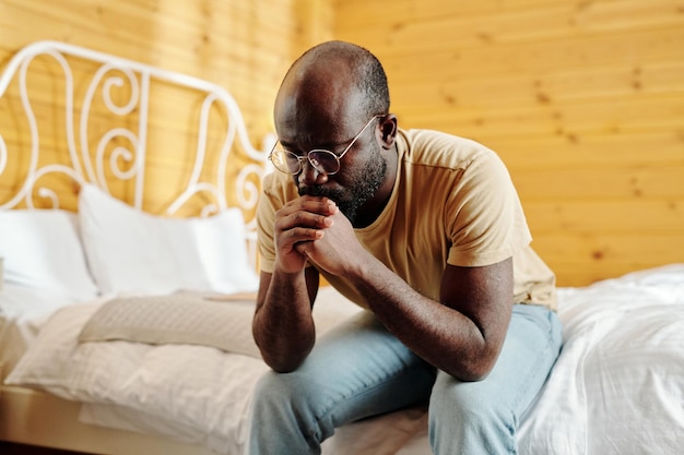 Giovane uomo di colore depresso che tiene le mani serrate vicino al viso