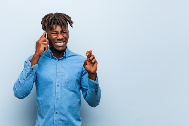 Giovane uomo di colore di rasta che tiene le dita di un incrocio del telefono per avere fortuna