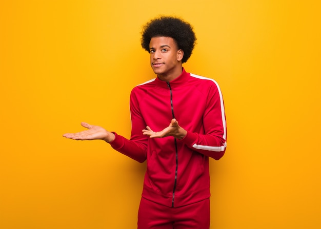 Giovane uomo di colore di sport sopra una parete arancione confusa e dubbiosa