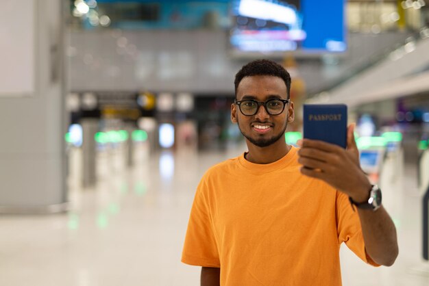 Giovane uomo di colore pronto a viaggiare al terminal dell'aeroporto e mostrando il passaporto