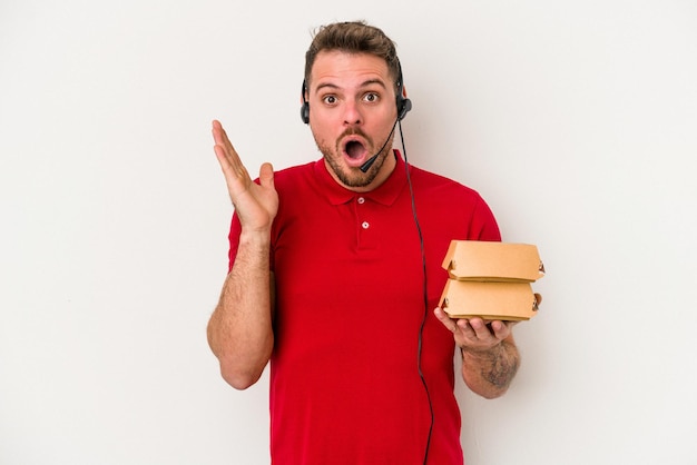 Giovane uomo di consegna caucasico che tiene un hamburger isolato su sfondo bianco sorpreso e scioccato.