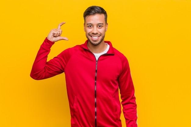 Giovane uomo di forma fisica filippina che tiene qualcosa poco con indici, sorridente e fiducioso.