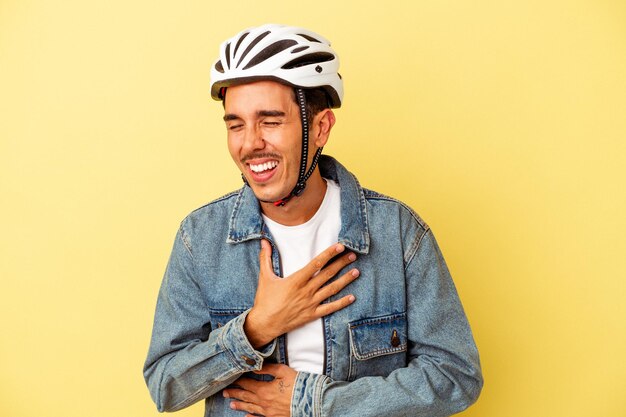 Giovane uomo di razza mista che indossa una bici da casco isolata su sfondo giallo ridendo e divertendosi.