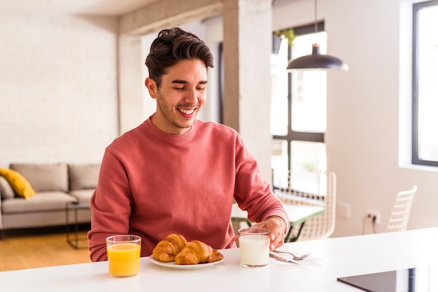 Giovane uomo di razza mista che mangia croissant in cucina la mattina