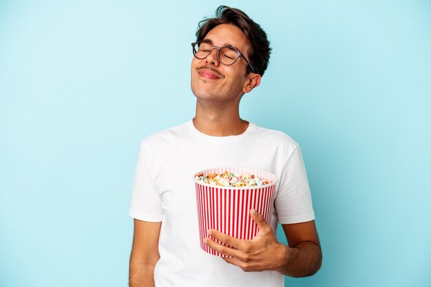 Giovane uomo di razza mista che mangia popcorn isolati su sfondo blu sognando di raggiungere obiettivi e scopi