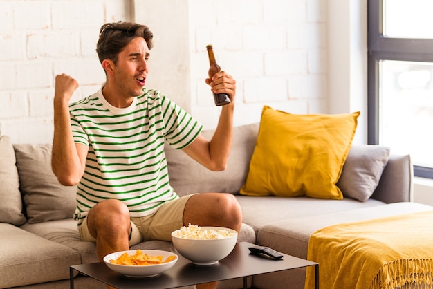 Giovane uomo di razza mista che mangia popcorn seduto sul divano