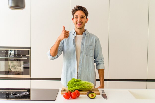 Giovane uomo di razza mista che prepara un'insalata per pranzo sorridendo e alzando il pollice