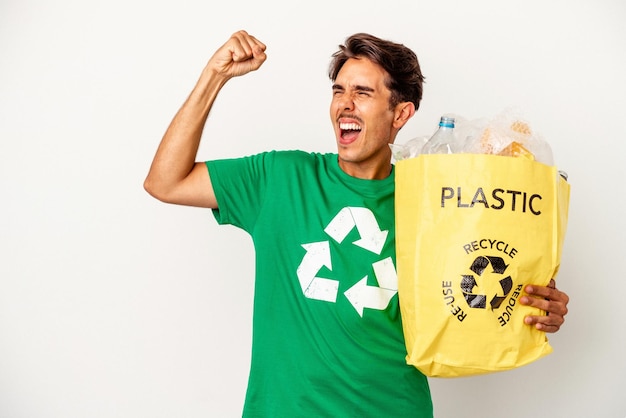 Giovane uomo di razza mista che ricicla plastica isolata su sfondo giallo alzando il pugno dopo una vittoria, concetto vincitore.