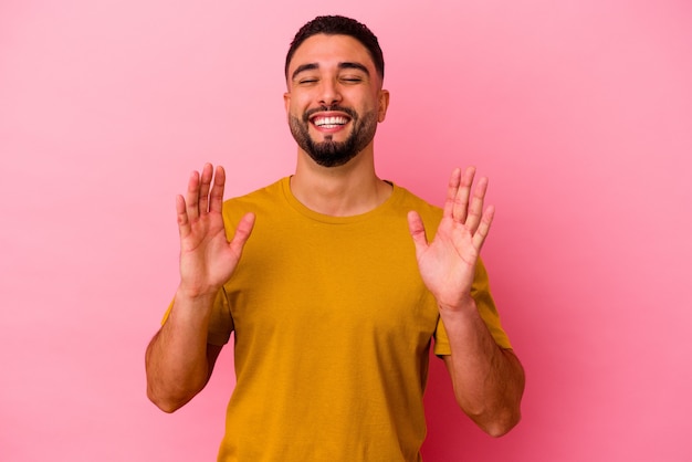 Giovane uomo di razza mista isolato sul muro rosa ride ad alta voce tenendo la mano sul petto.