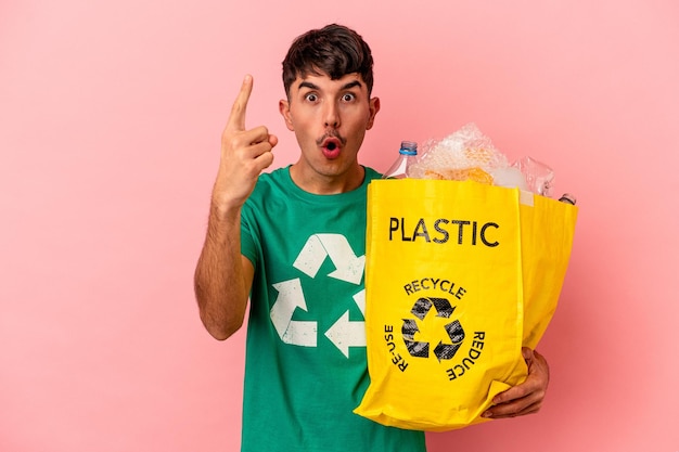 Giovane uomo di razza mista plastica riciclata isolata su sfondo rosa con un'idea, un concetto di ispirazione.