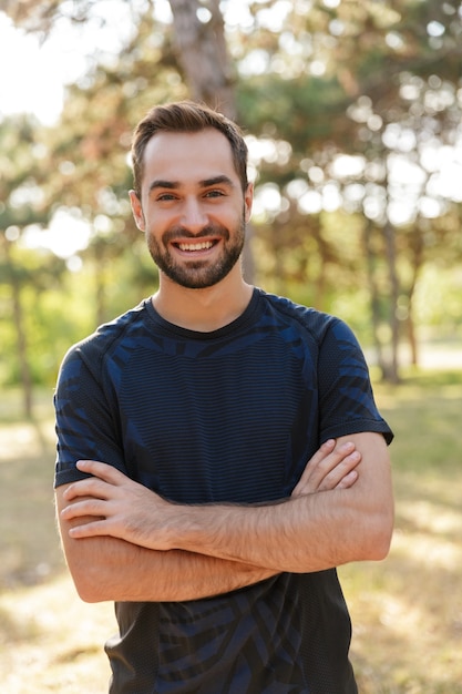 giovane uomo di sport allegro ottimista positivo forte che posa all'aperto nel parco verde della natura.