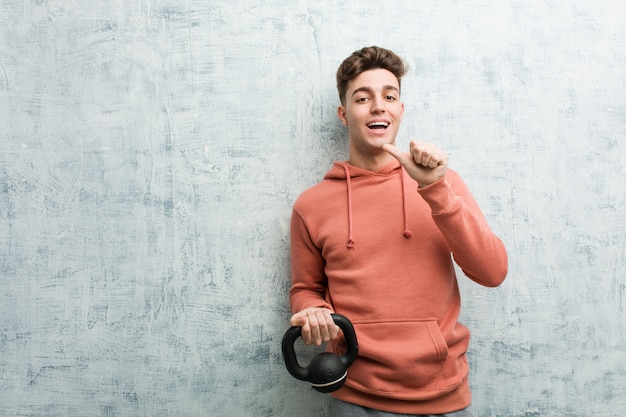 Giovane uomo di sport che tiene una testa di legno che sorride allegramente indicando con l'indice via.