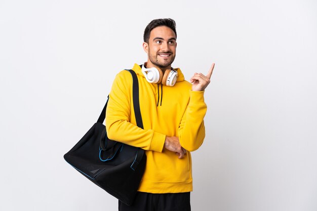 Giovane uomo di sport con borsa sportiva isolato sul muro bianco rivolto verso l'alto una grande idea