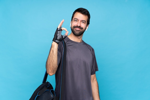 Giovane uomo di sport con la barba sopra la parete blu isolata che mostra segno giusto con le dita