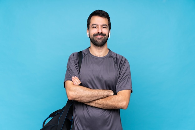 Giovane uomo di sport con la barba sopra la parete blu isolata mantenendo le braccia incrociate in posizione frontale