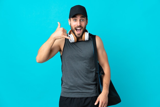 Giovane uomo di sport con la borsa di sport isolata sulla parete blu che fa gesto del telefono. Richiamami segno