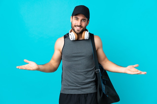 Giovane uomo di sport con la borsa di sport isolata sulla parete blu che ha dubbi