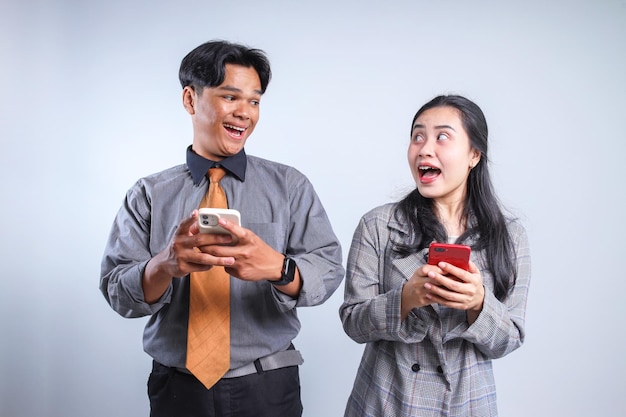 Giovane uomo e donna asiatici in abiti formali con gli smartphone in mano e che si guardano l'un l'altro con felicità